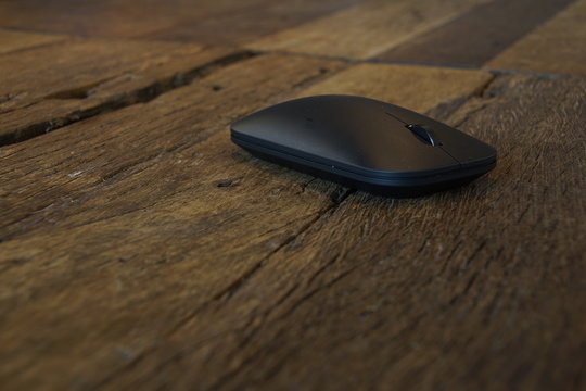 A Black Bluetooth Mouse On A Scratch Surface Wooden Table