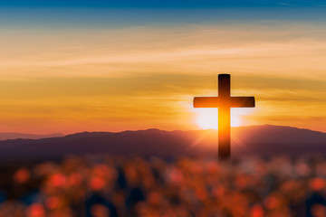 Silhouette of cross on mountain sunset background.