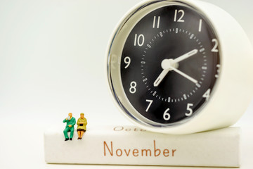 Miniature people: Happy senior couple standing on white wooden box with clock. Retirement, emergency plan Concept.