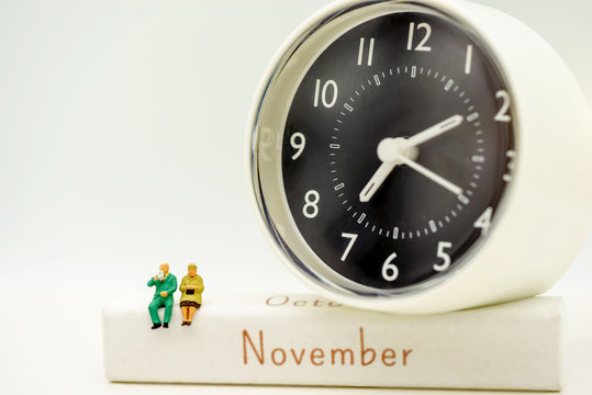 Miniature people: Happy senior couple standing on white wooden box with clock. Retirement, emergency plan Concept.