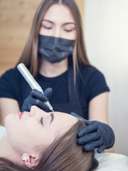 Master at work with the eyebrows makes microbleeding tattoo . Microblading eyebrows workflow in a beauty salon. Light brown girl do eyebrows needle.