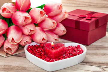 Festive background to the Valentine's day. A bouquet of tulips, a gift box, a heart-shaped plate and a heart-shaped candle. On a wooden background.