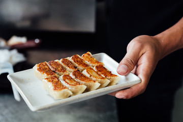 Chef is holding a plate of Yaki-Gyoza set (Japanese Pan-Fried Dumplings) after cooked. Hot, fresh, juicy and tasty.