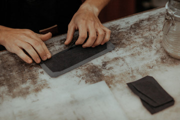 Close up of leather craftsman working with natural leather. Handmade master at work in local workshop. Handmade concept.