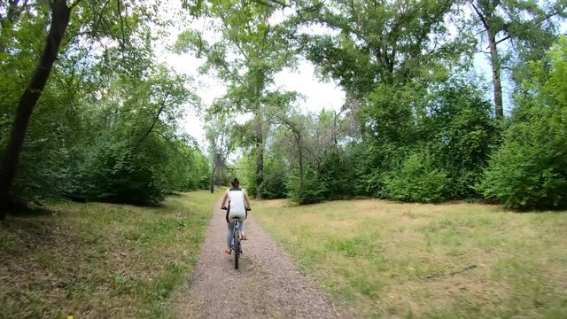 Cycling in the park. Girl riding a bike on a forest trail. Back view. Slow motion