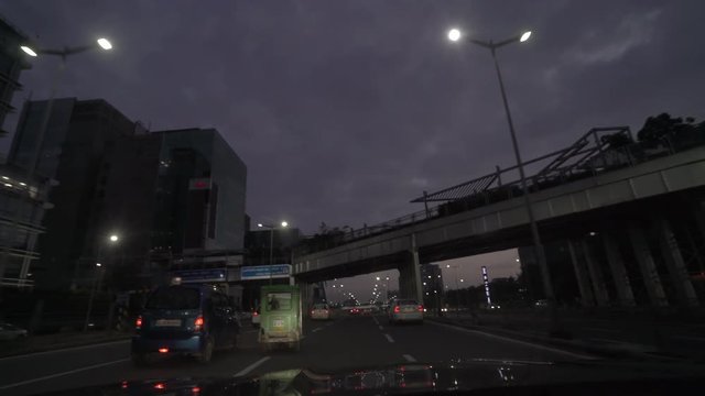Car's pov through a wide road with commercial, financial and business headquarters in contemporary glass building as the sun is setting and the lights have come one