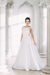 Fototapeta premium Beautiful girl in a wedding dress with a bouquet. Bride in a bright Sunny Studio.