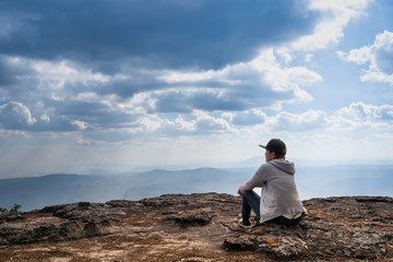 A person sitting  on rocky mountain looking out at scenic natural view and beautiful blue sky