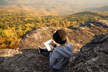 A woman sitting reading and writing looking out at beautiful natural view