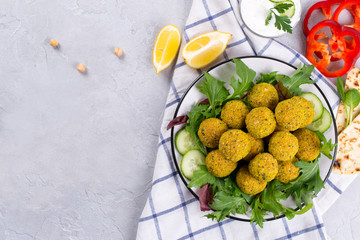 Homemade spicy chickpea falafel garnished with fresh vegetable and yogurt on a plate over light concrete background. Israeli cuisine concept