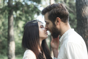 Obraz premium Young beautiful Slavic couple in love walks through the woods, sweet girl in a simple boho-style wedding dress. They are happy and calm. Golden hour, summer day, warm. They kiss, hug and hold hands.