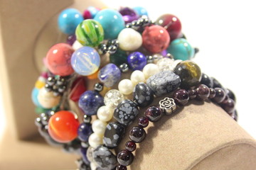 Many handmade jewelry with natural semi-precious stones. Bracelets on a stand on a white background. Lapis lazuli, amethyst, turquoise, coral, garnet.