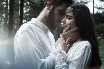 Young beautiful Slavic couple in love walks through the woods, sweet girl in a simple boho-style wedding dress. They are happy and calm. Golden hour, summer day, warm. They kiss, hug and hold hands.