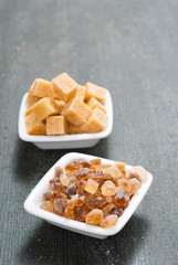 brown cubes and rock sugar on white square dishes, dark wood table