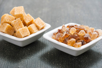 brown cubes and rock sugar on white square dishes, dark wood table