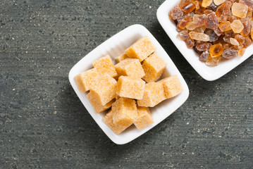 brown cubes and rock sugar on white square dishes, dark wood table