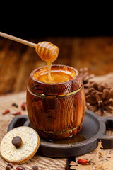 Honey pouring from a honey stick to a wooden barrel.