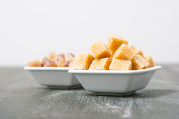brown cubes and rock sugar on white square dishes, dark wood table