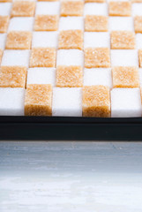 white and brown sugar nubs on black square plate, bright wood table background