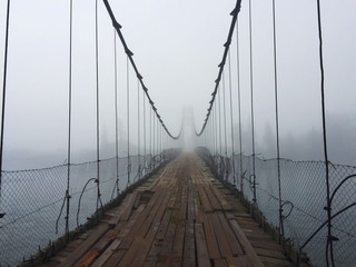 Old suspension bridge entrance in fog. Altai village bridge. Early misty morning