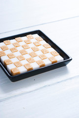 white and brown sugar nubs on black square plate, bright wood table background