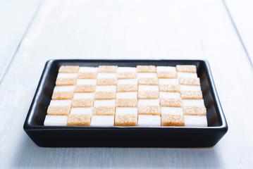 white and brown sugar nubs on black square plate, bright wood table background