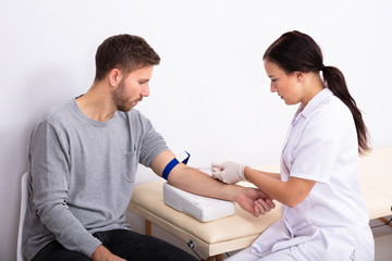 Doctor Injecting Patient With Syringe To Collect Blood