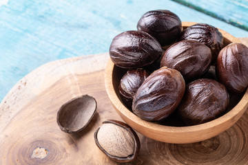 Whole nutmeg nuts in a bowl on blue rustic wooden table.
