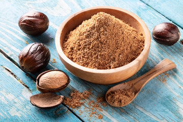 Whole inshell nut and nutmeg powder in a wooden bowl and spoon on old blue rustic background. - obrazy, fototapety, plakaty