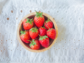 Strawberry in a wooden cup on white lace fabric texture.