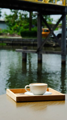 Hot latte coffee in white cup on table beside river and space for write wording, served in a shop beside the river in a relax time with space for write wording, good environment for meet friend