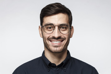 Obraz premium Smart businessman smiling at camera, wearing round glasses, isolated on gray background