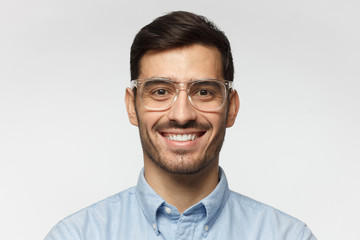 Smart businessman smiling at camera, wearing trendy transparent glasses, isolated on gray background