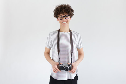Young female with photo camera hanging on strap on her neck, smiling as if ready to take pictures