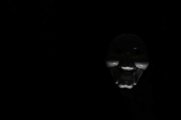 White scary mask on a black background with whites hand.