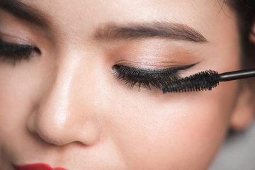 An asian woman applying mascara on her eyelashes