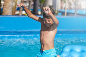 European boy jumping into water from inflatable mattress in swimming pool.