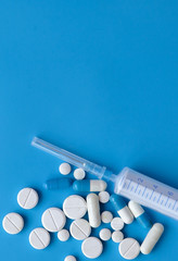 Assorted medical drugs and syringe on blue background, with copy space
