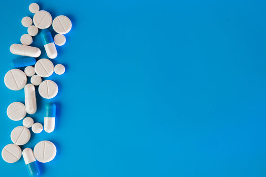 Scattered white pills on blue table. Mock up for special offers as advertising, web background or other ideas. Medical, pharmacy and healthcare concept. Copy space. Empty place for text or logo