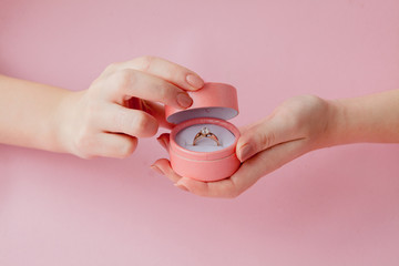 Woman opens a gift box with jewellery. Wedding ring in a box in the hands of women on a pink...