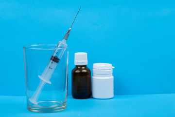 Syringe in a glass, white small bottle on a blue background.  Brown bottle
