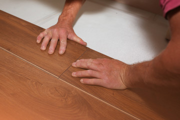Worker is making laminate flooring in apartment. Maintenance repair works renovation in the flat. Restoration of wooden parquet floor planks indoors.