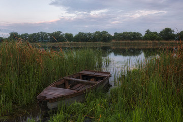 Sunrise on a quiet river. A wooden boat stands on the shore in the reeds.