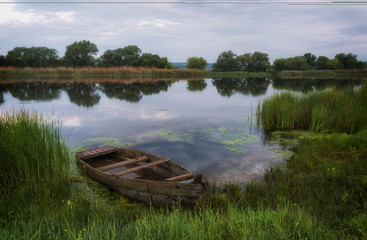 Obraz premium Spring morning on the river Southern Bug. At the coast in the reeds is a wooden boat.