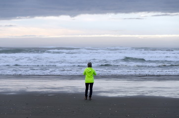 Hiker in electric windbreaker walking at sunset  on a sand beach