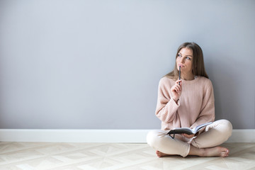 Young woman with notepad think hard sitting on a wooden floor.