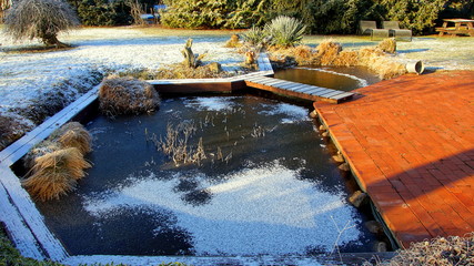 romantischer Gartenteich mit Holzbrücke an sonnigem Wintertag