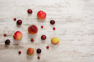 A circle of fruits, apple, peach, plum, raspberry, lie on a textured light wooden background. Flat top view, place for text. Flat Lay, Copy Space. Summer background.