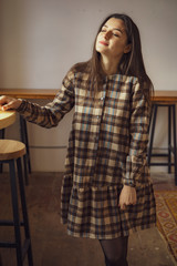 French wear style. How wear checkered dress like fashion girl. Girl, woman with long black hair posing in old cafe background. Fashionable brunette female.
