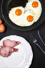 Fried eggs and bacon on a dark background seen from above